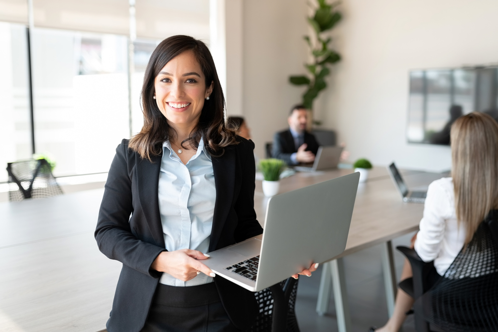 Portrait,Of,Smiling,Female,Entrepreneur,Holding,A,Laptop,With,Team